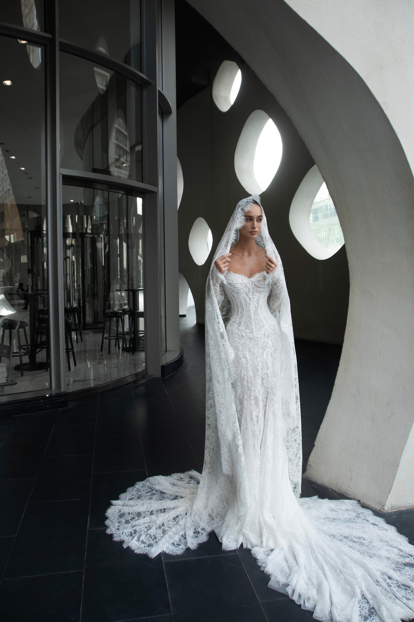Off-shoulder lace wedding gown with long illusion sleeves, corset bodice, and chapel-length train.