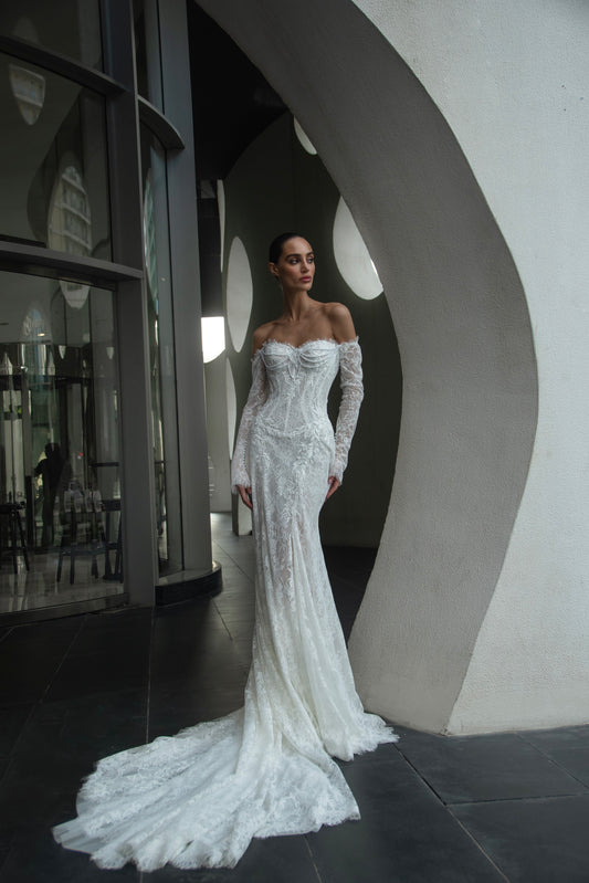 Off-shoulder lace wedding gown with long illusion sleeves, corset bodice, and chapel-length train.