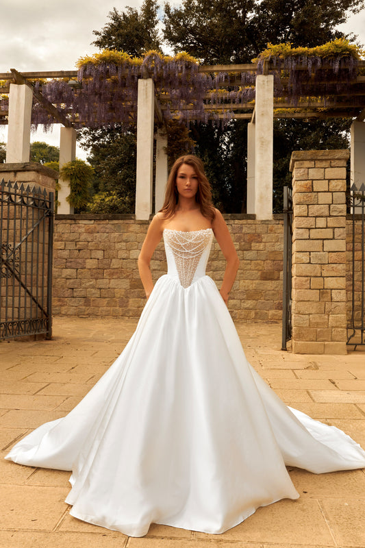 Bride in princess-style sleeveless A-line wedding gown with boat neckline, illusion deep-V pearl and sequin embroidered bodice, satin skirt, and cathedral train.