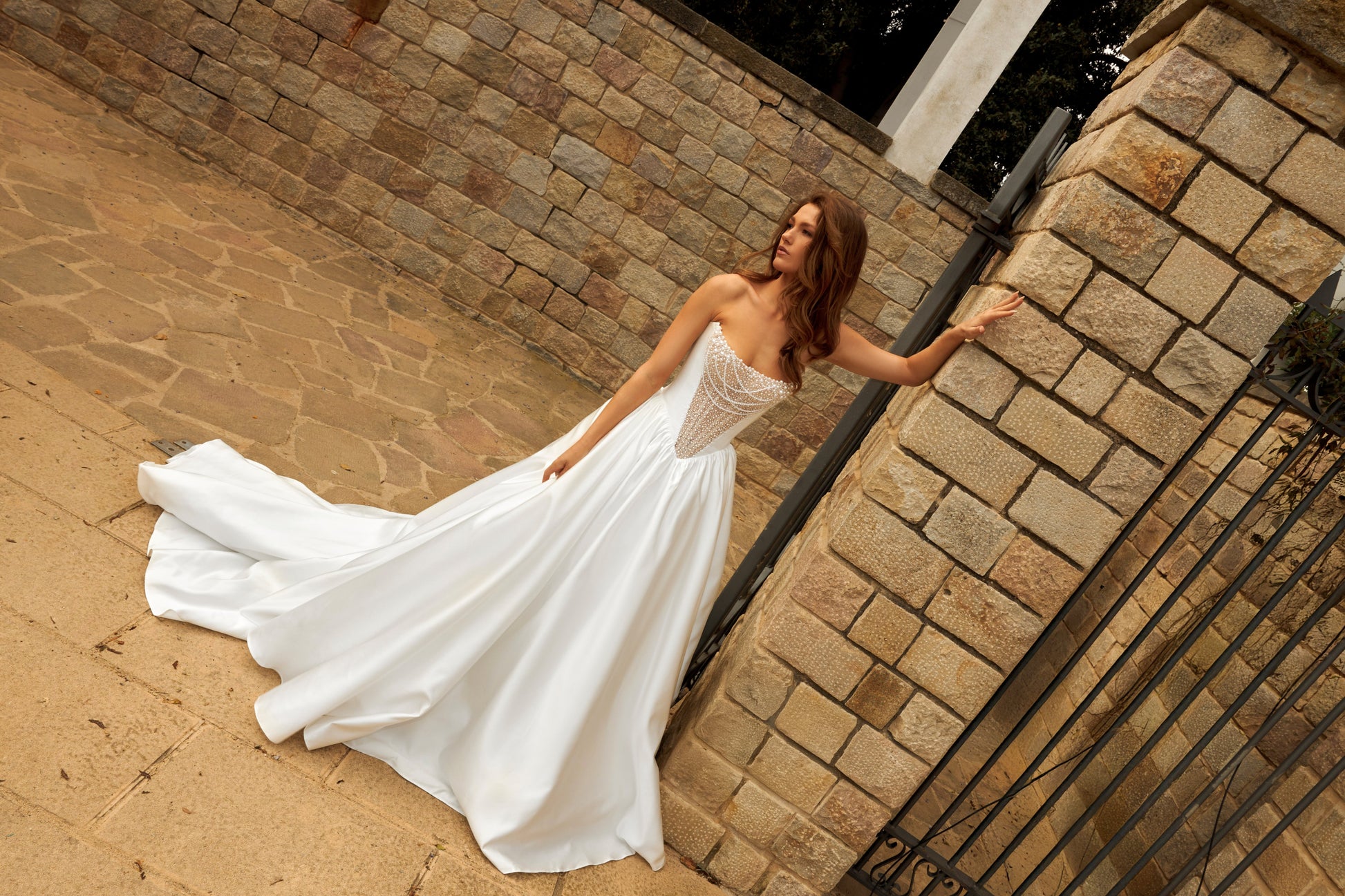 Bride in princess-style sleeveless A-line wedding gown with boat neckline, illusion deep-V pearl and sequin embroidered bodice, satin skirt, and cathedral train.