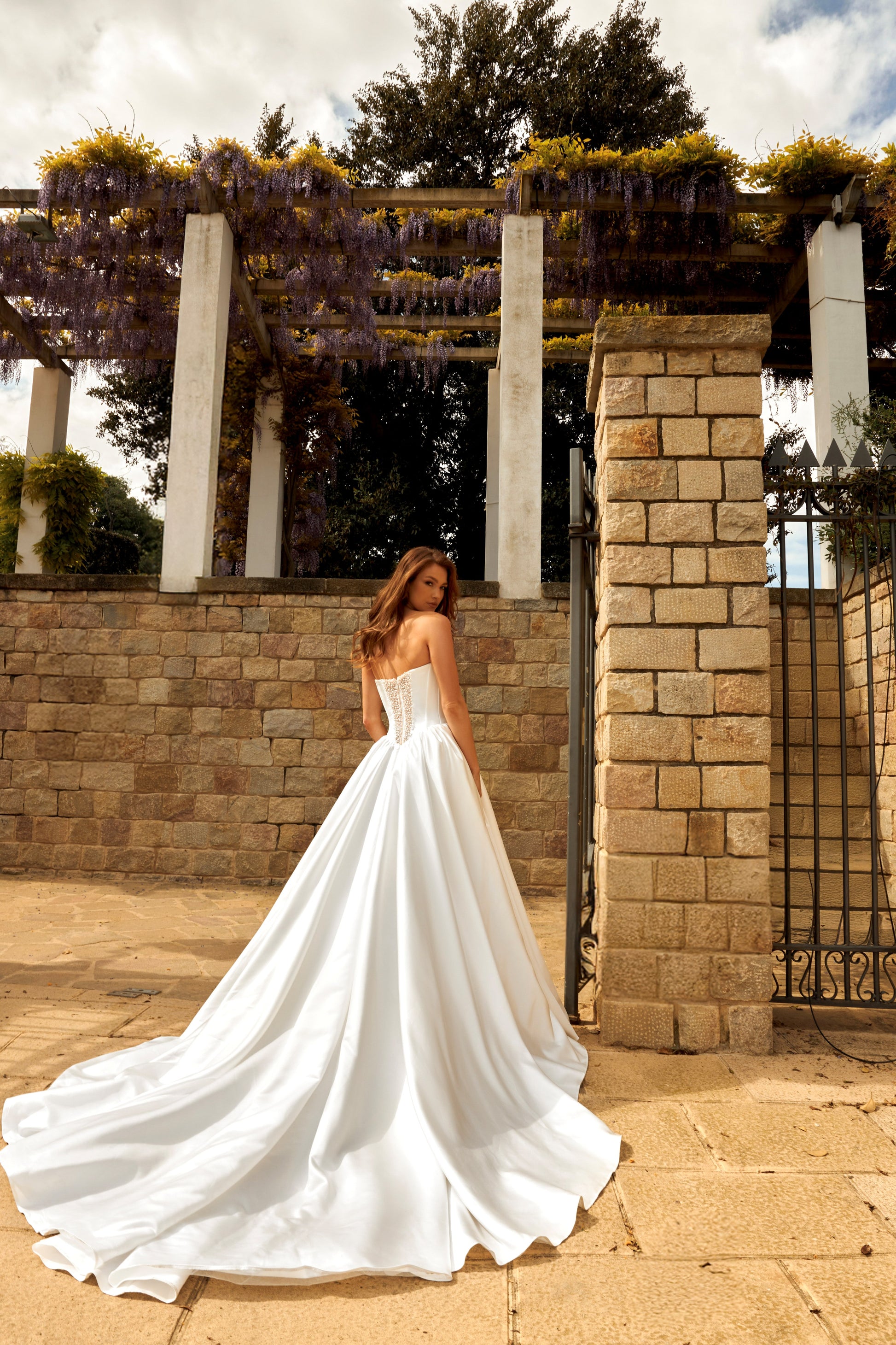 Bride in princess-style sleeveless A-line wedding gown with boat neckline, illusion deep-V pearl and sequin embroidered bodice, satin skirt, and cathedral train.
