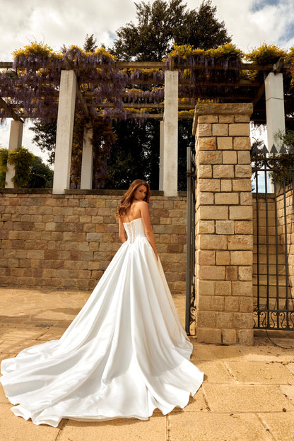 Bride in princess-style sleeveless A-line wedding gown with boat neckline, illusion deep-V pearl and sequin embroidered bodice, satin skirt, and cathedral train.