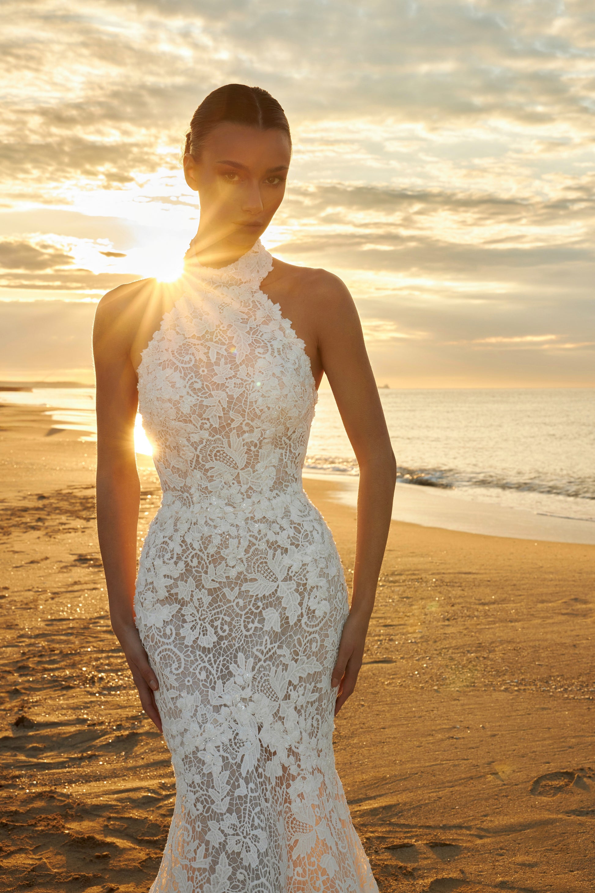 Bride wearing sleeveless halter neckline lace mermaid wedding gown with open back, fitted silhouette, zip closure, and sweep train.