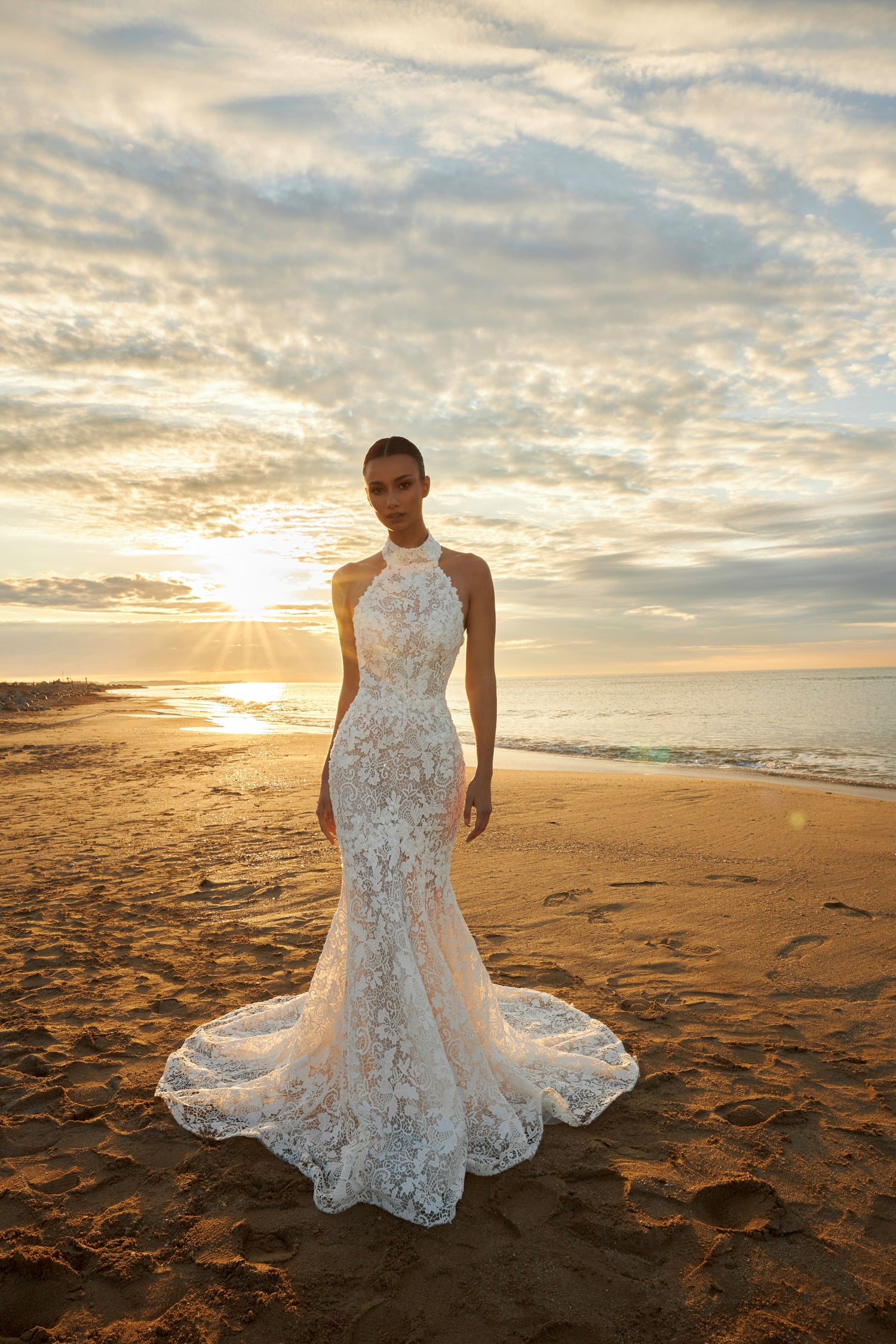 Bride wearing sleeveless halter neckline lace mermaid wedding gown with open back, fitted silhouette, zip closure, and sweep train.