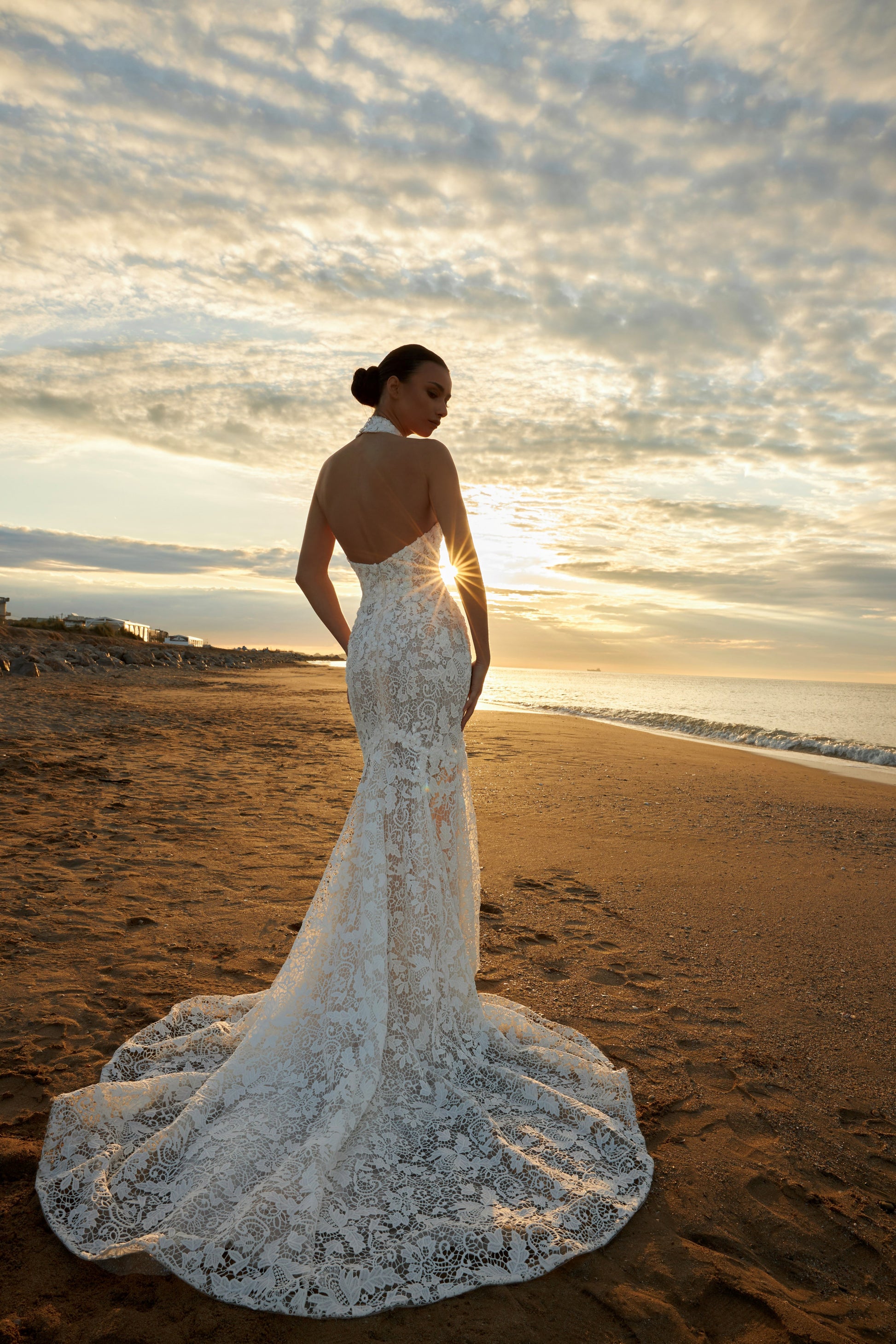 Bride wearing sleeveless halter neckline lace mermaid wedding gown with open back, fitted silhouette, zip closure, and sweep train.