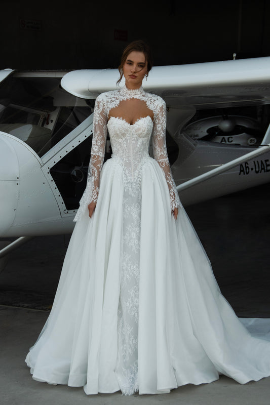 Bride wearing Leontine lace long-sleeve wedding dress with high illusion neckline, fitted corset bodice, and chapel train, featuring intricate lace cuffs and back detailing.