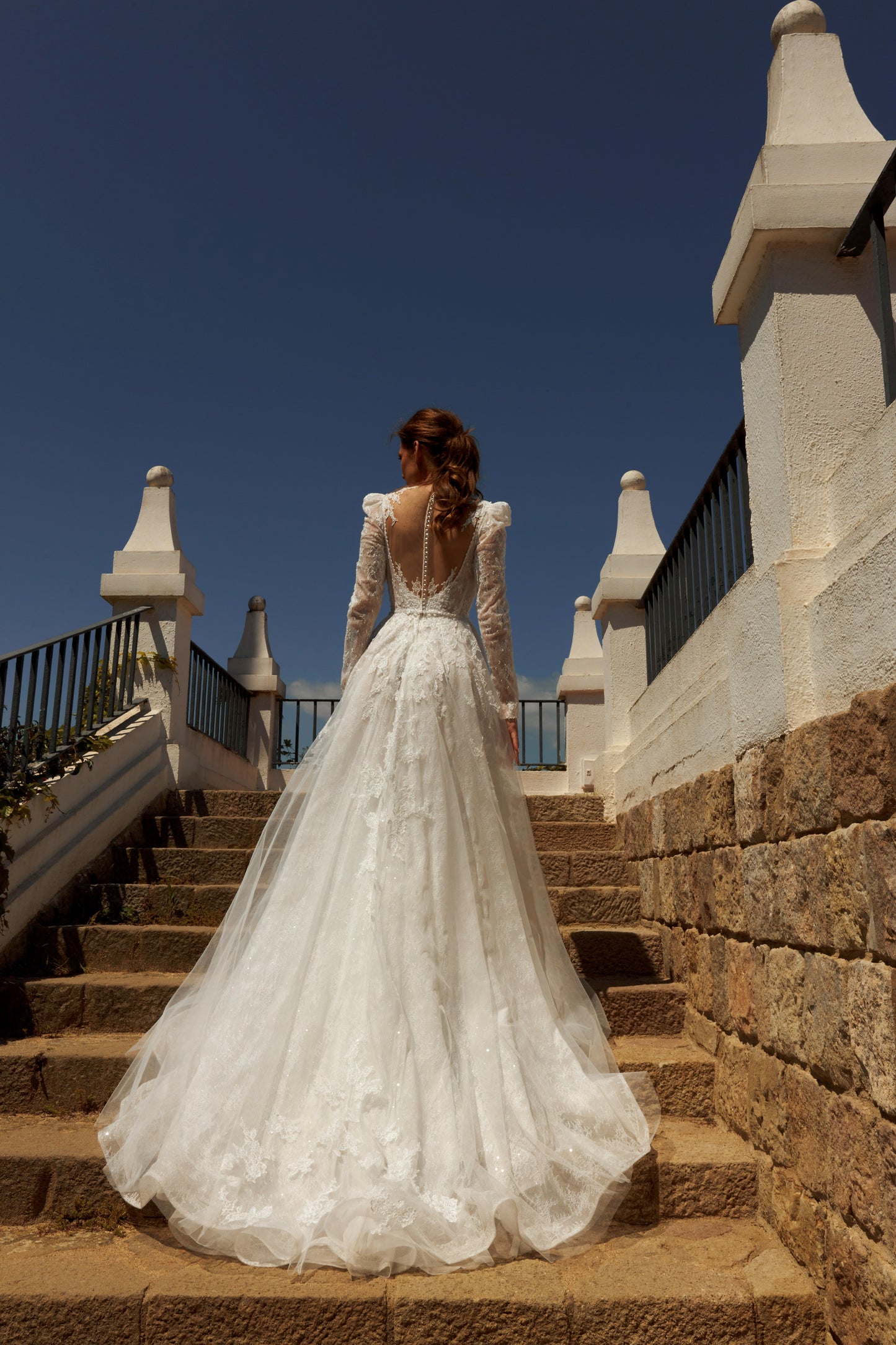 Bride in long sleeve lace A-line bridal gown with puffy shoulders, illusion deep-V back, button closure, and chapel train.