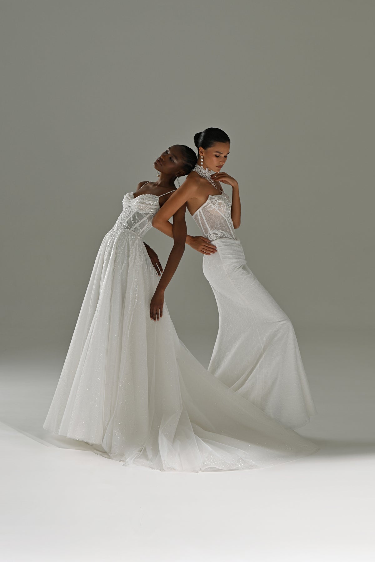 Lace sheath wedding dress with sheer cape – two brides embracing with the cape and train flowing