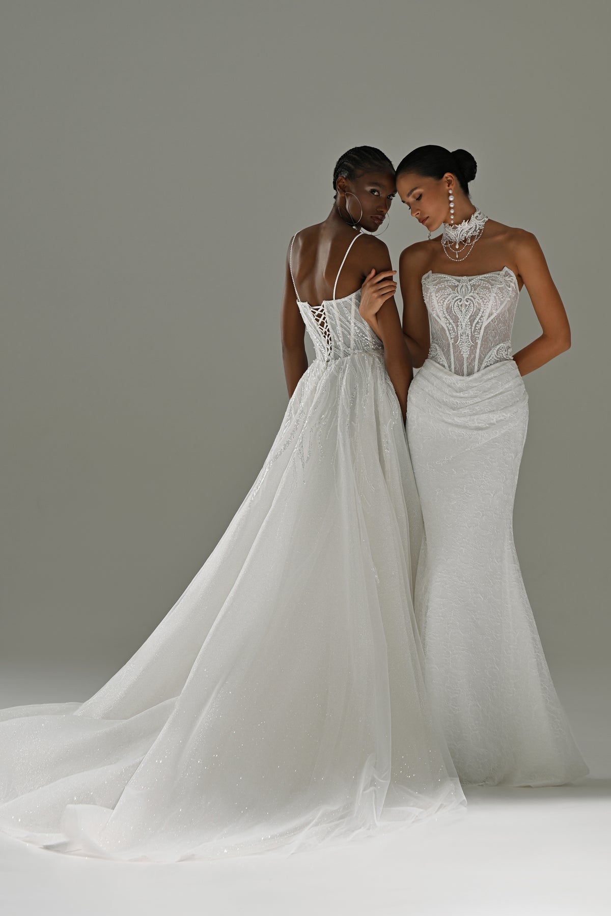 Lace sheath wedding dress with sheer cape – two brides standing together, full-length view