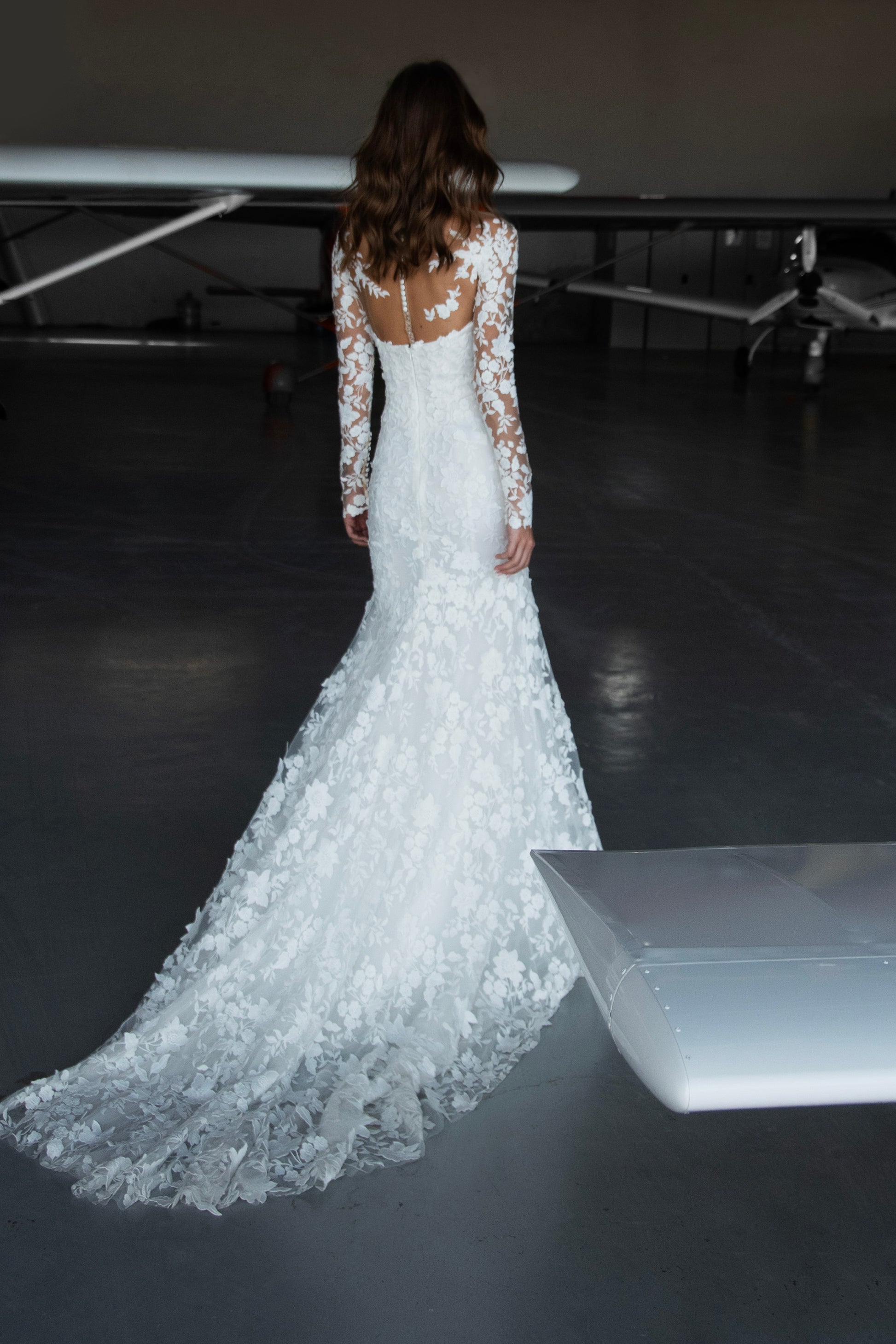 Bride in long-sleeve lace fit-and-flare wedding dress with floral appliqués, illusion back, and chapel train; styled with optional satin off-shoulder wrap.