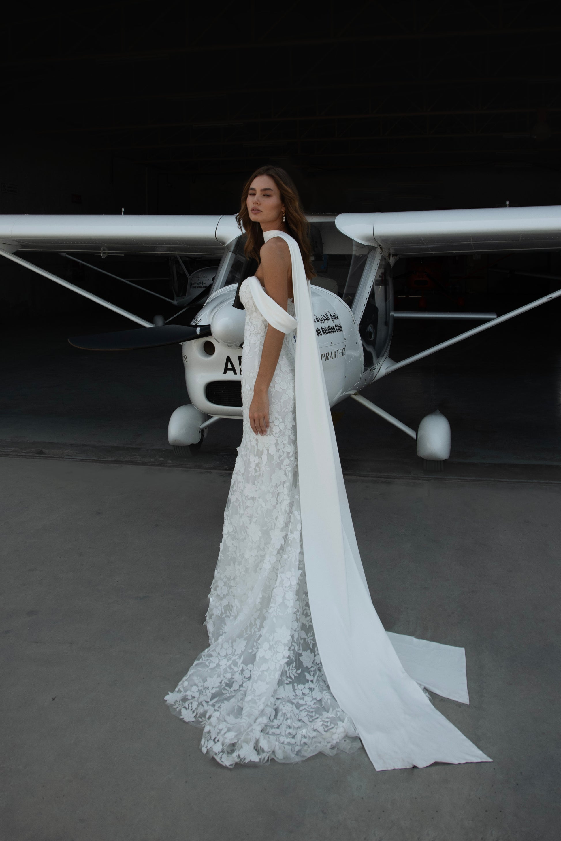 Bride in long-sleeve lace fit-and-flare wedding dress with floral appliqués, illusion back, and chapel train; styled with optional satin off-shoulder wrap.