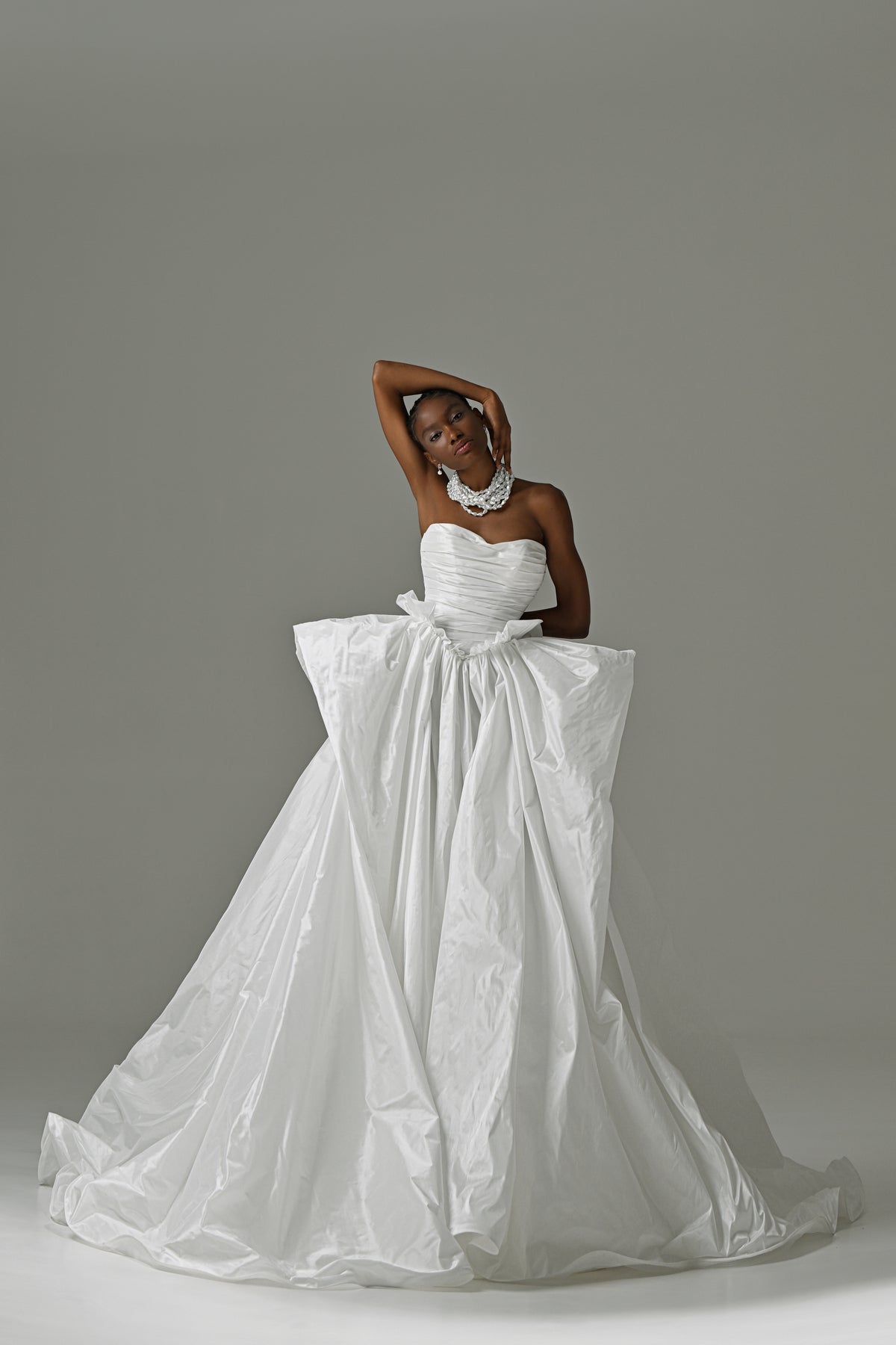 Strapless taffeta ball gown wedding dress with ruched bodice and oversized bow – full-length front view, arms overhead