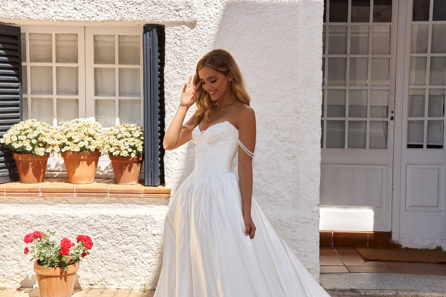 Bride wearing sleeveless satin A-line bridal gown with sweetheart neckline, pearl straps, drop-down waist, zip closure, open back, and chapel train.