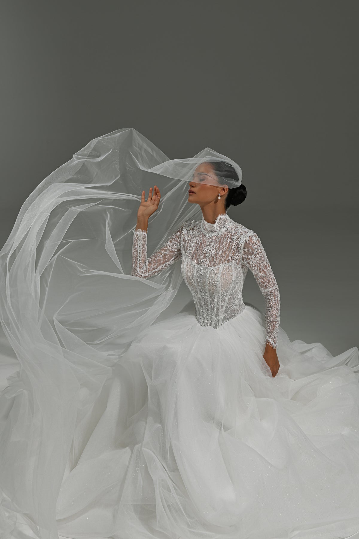 Lace high-neck wedding dress with corset bodice – model seated in the voluminous tulle skirt with the veil flowing