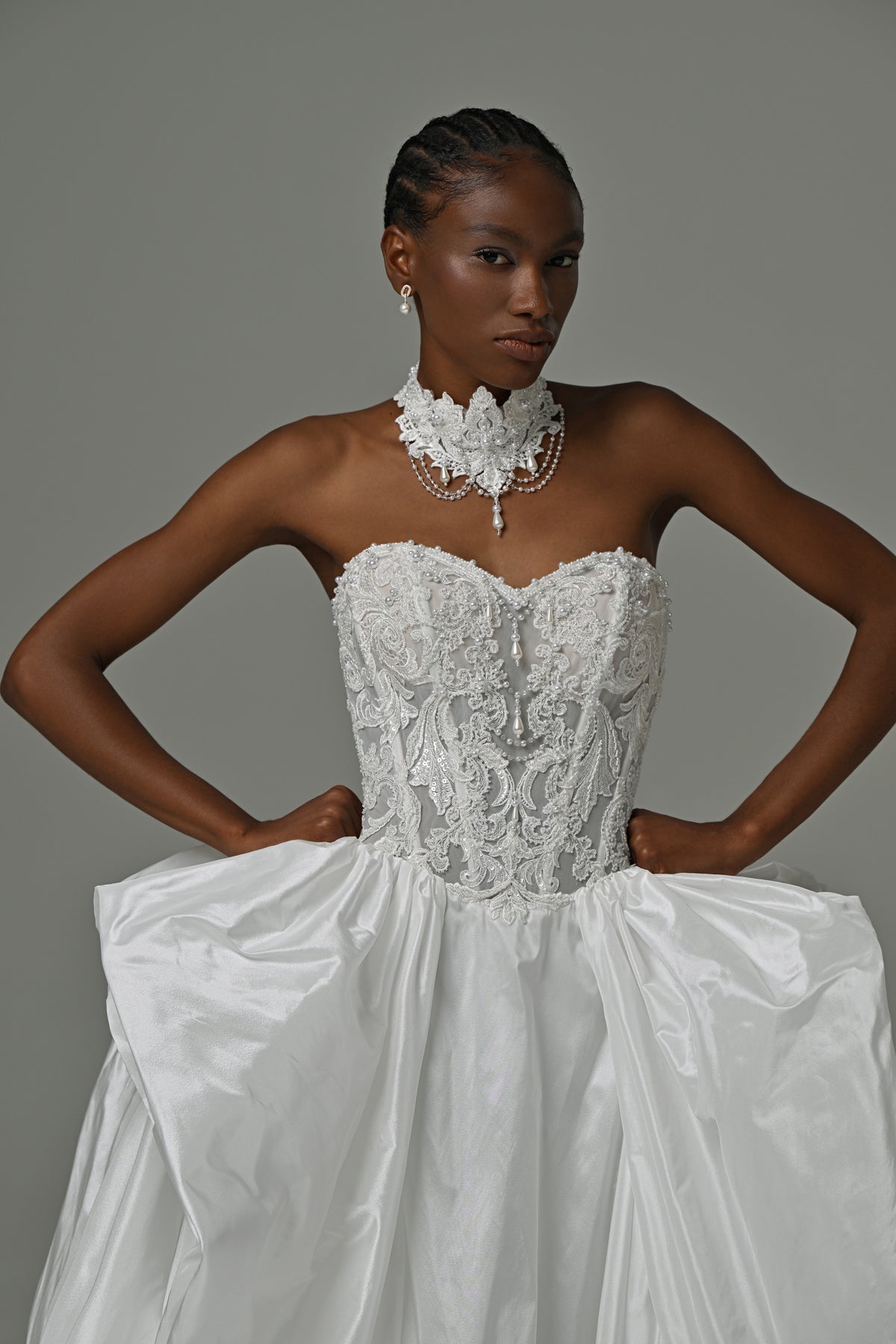 Strapless taffeta ball gown wedding dress with lace corset bodice and oversized bow skirt – front close-up, hands on hips