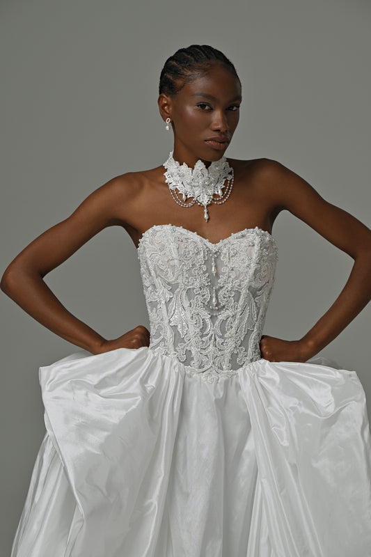 Strapless taffeta ball gown wedding dress with lace corset bodice and oversized bow skirt – front close-up, hands on hips