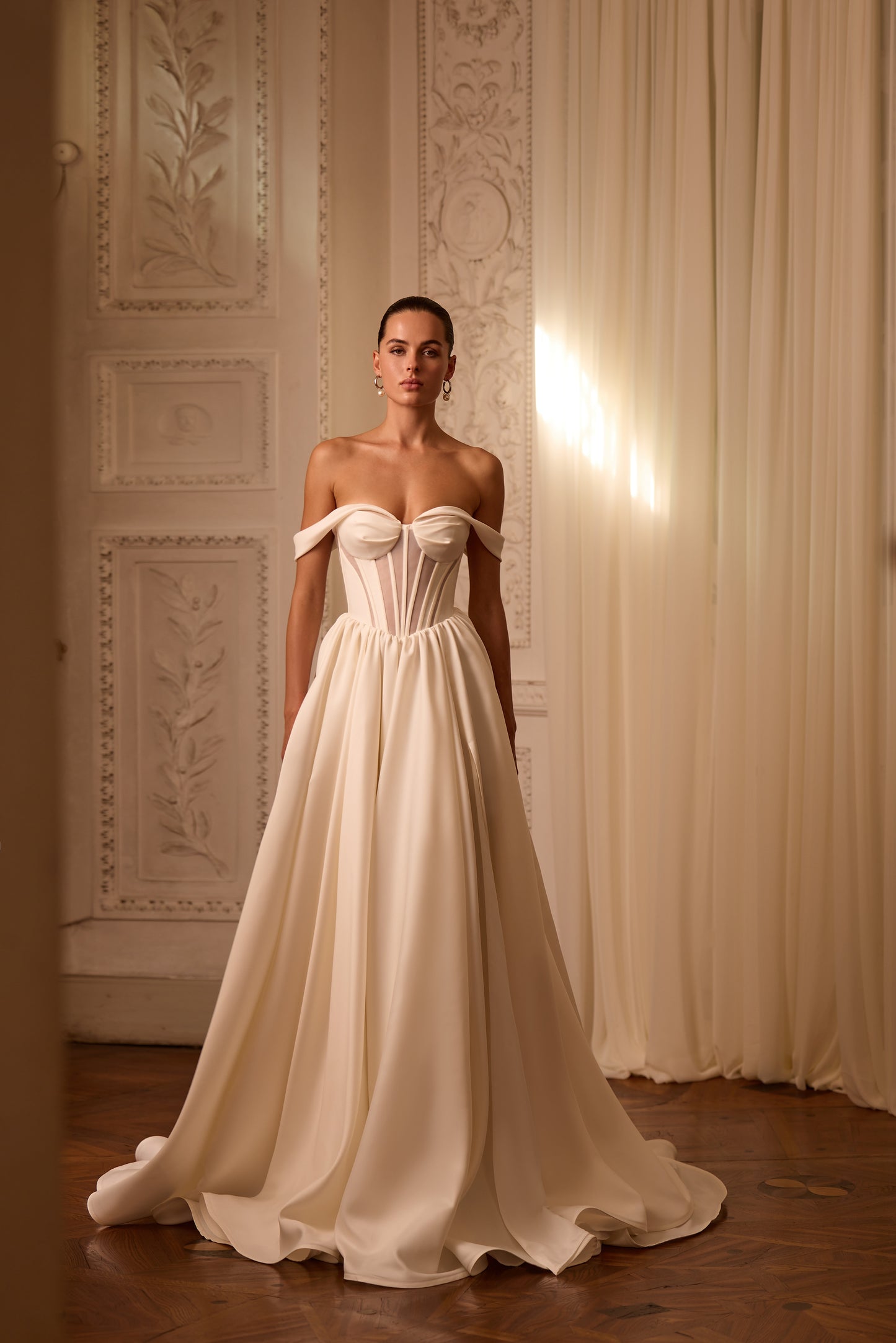 Bride in modern A-line wedding dress with structured V-shape corset bodice, sleeveless off-the-shoulder neckline, and lace-up back.

