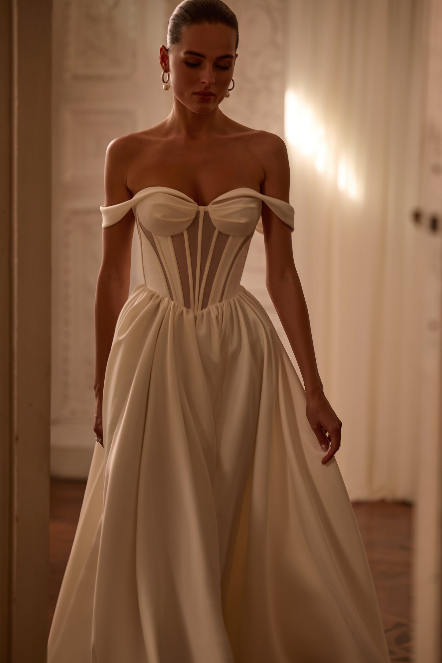 Bride in modern A-line wedding dress with structured V-shape corset bodice, sleeveless off-the-shoulder neckline, and lace-up back.


