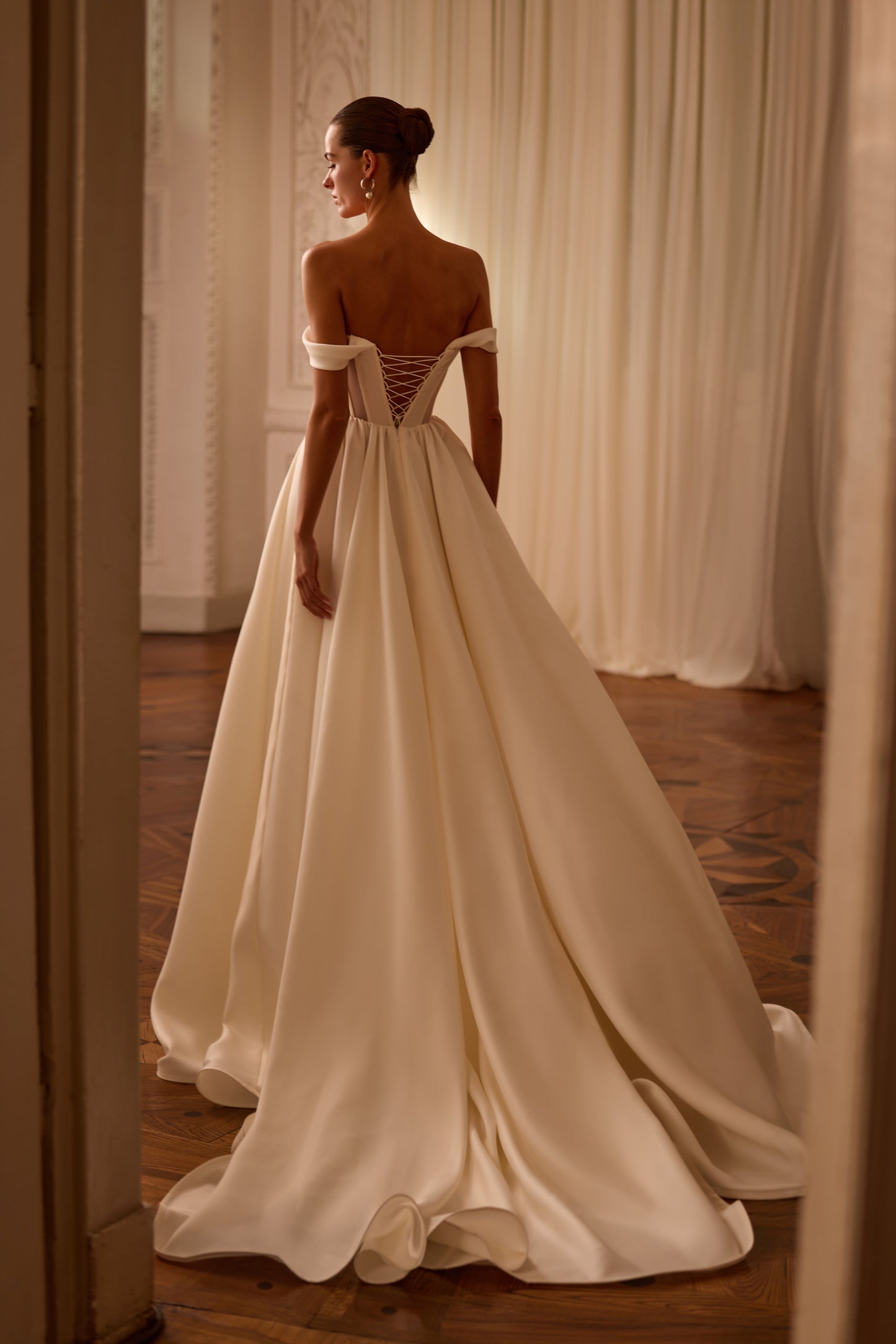 Bride in modern A-line wedding dress with structured V-shape corset bodice, sleeveless off-the-shoulder neckline, and lace-up back.

