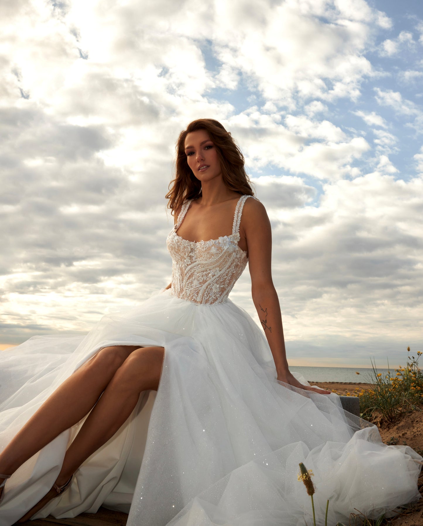 Sleeveless A-line bridal gown with boat neckline, lace bodice, wide straps, square back, glitter tulle slit skirt, and chapel train.