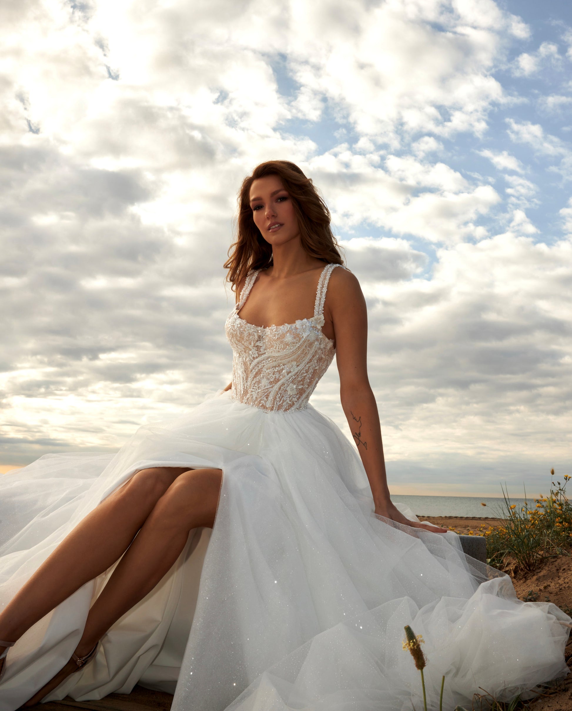 Sleeveless A-line bridal gown with boat neckline, lace bodice, wide straps, square back, glitter tulle slit skirt, and chapel train.