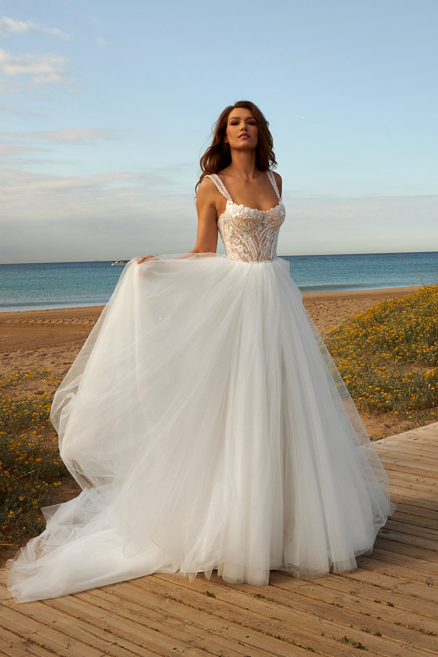 Sleeveless A-line bridal gown with boat neckline, lace bodice, wide straps, square back, glitter tulle slit skirt, and chapel train.