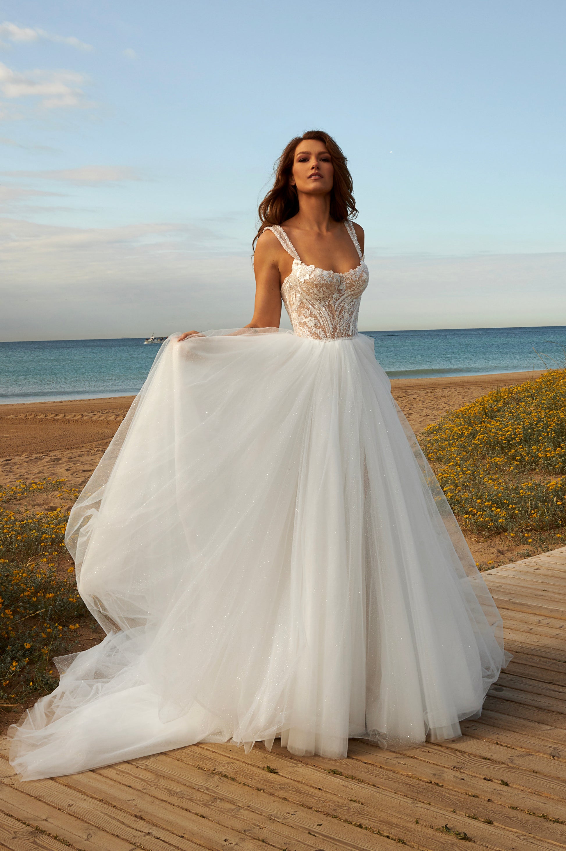 Sleeveless A-line bridal gown with boat neckline, lace bodice, wide straps, square back, glitter tulle slit skirt, and chapel train.