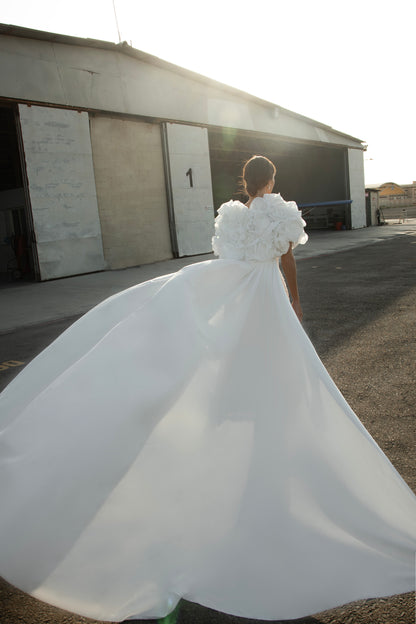 Bride wearing short beaded mini wedding dress with voluminous floral bolero and detachable satin train, photographed at sunset airfield.
