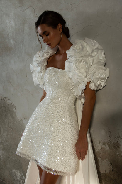 Bride wearing short beaded mini wedding dress with voluminous floral bolero and detachable satin train, photographed at sunset airfield.