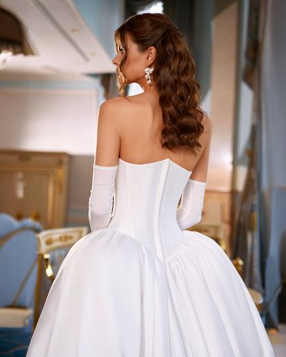 Mikado A-line wedding dress with reverse sweetheart neckline, drop-down waspie corset, sleeveless design, long gloves, zip closure, and flowing chapel train for elegant modern bridal look
