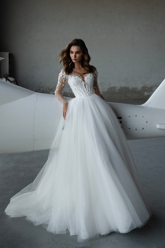 Bride wearing illusion tulle ball gown with 3D floral appliqués, pearl embroidery, and illusion back with buttons, photographed beside an airplane hangar.