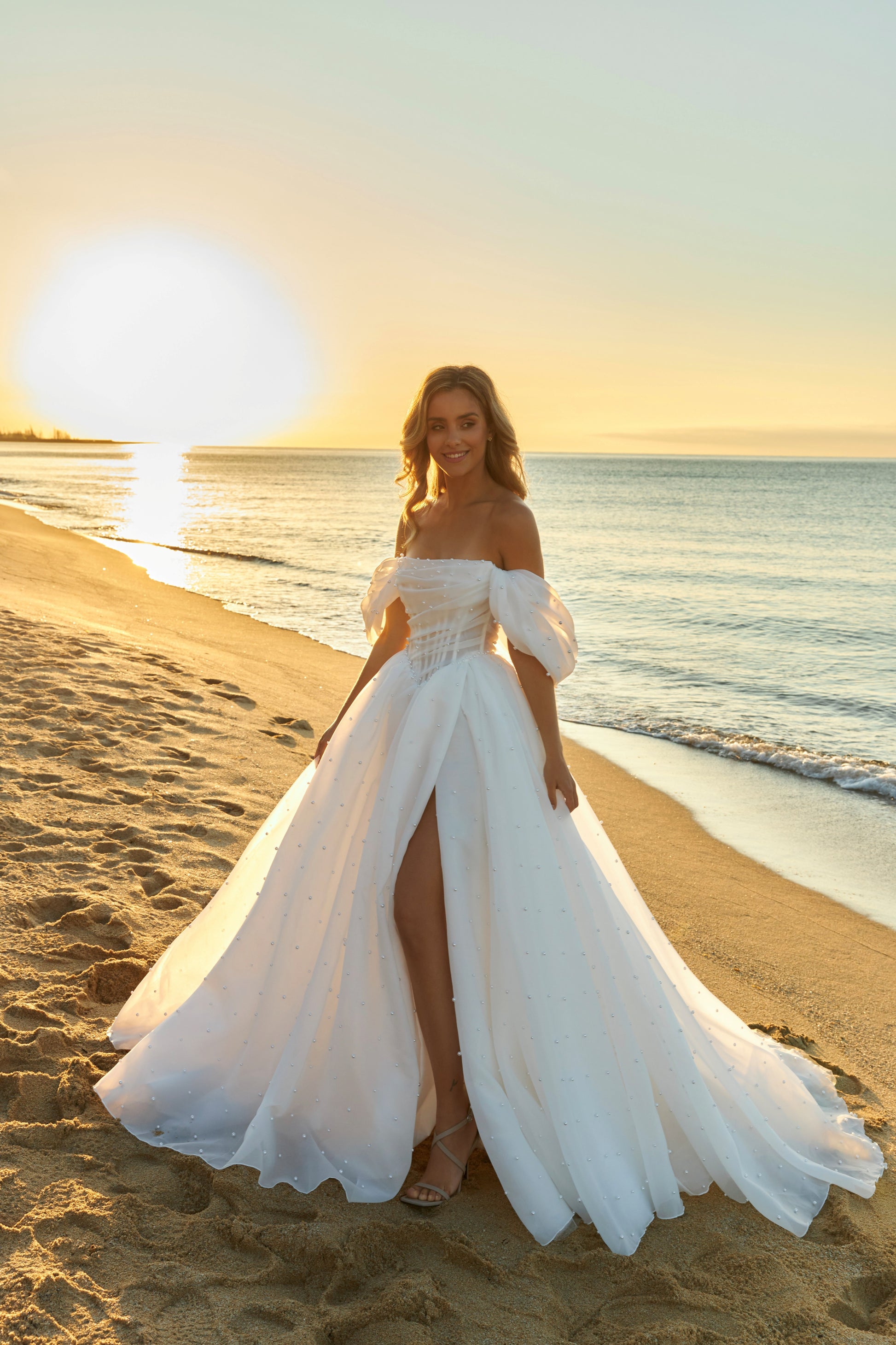 Princess A-line organza bridal gown with short off-the-shoulder draped sleeves, pearl details, slit skirt, drop-down waist, and chapel train.