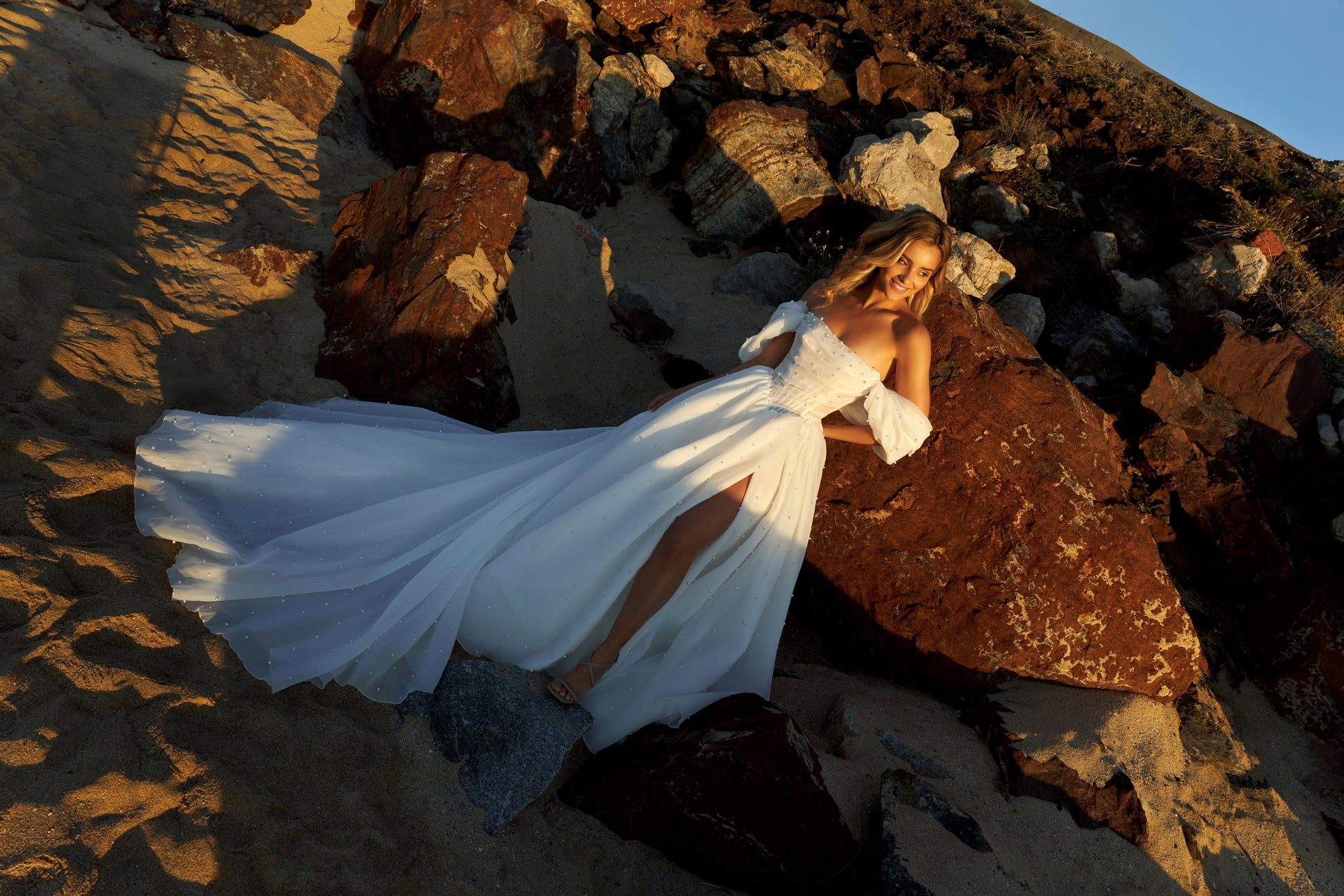 Princess A-line organza bridal gown with short off-the-shoulder draped sleeves, pearl details, slit skirt, drop-down waist, and chapel train.