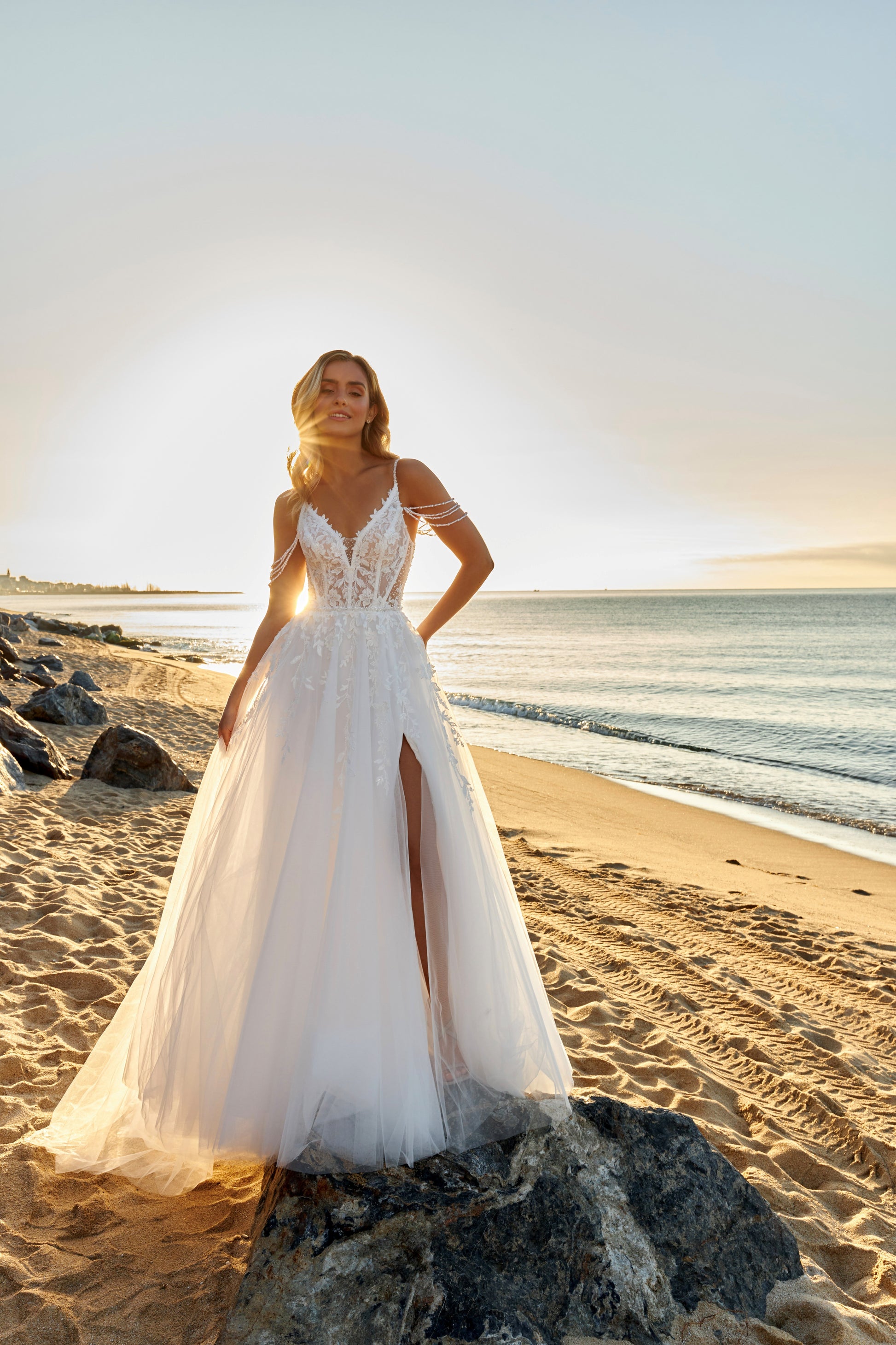 Sleeveless A-line lace bridal gown with spaghetti straps, deep-V neckline, open V-back, slit tulle skirt, and chapel train.