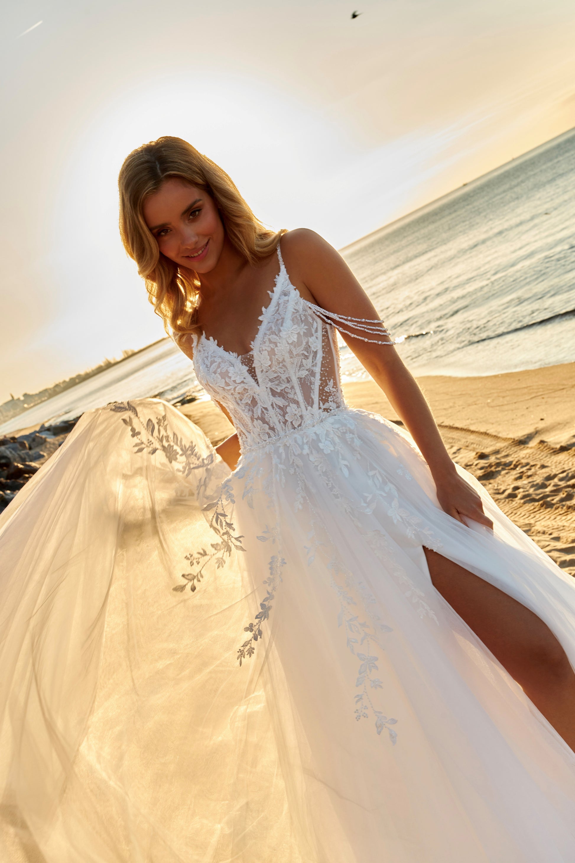 Sleeveless A-line lace bridal gown with spaghetti straps, deep-V neckline, open V-back, slit tulle skirt, and chapel train.
