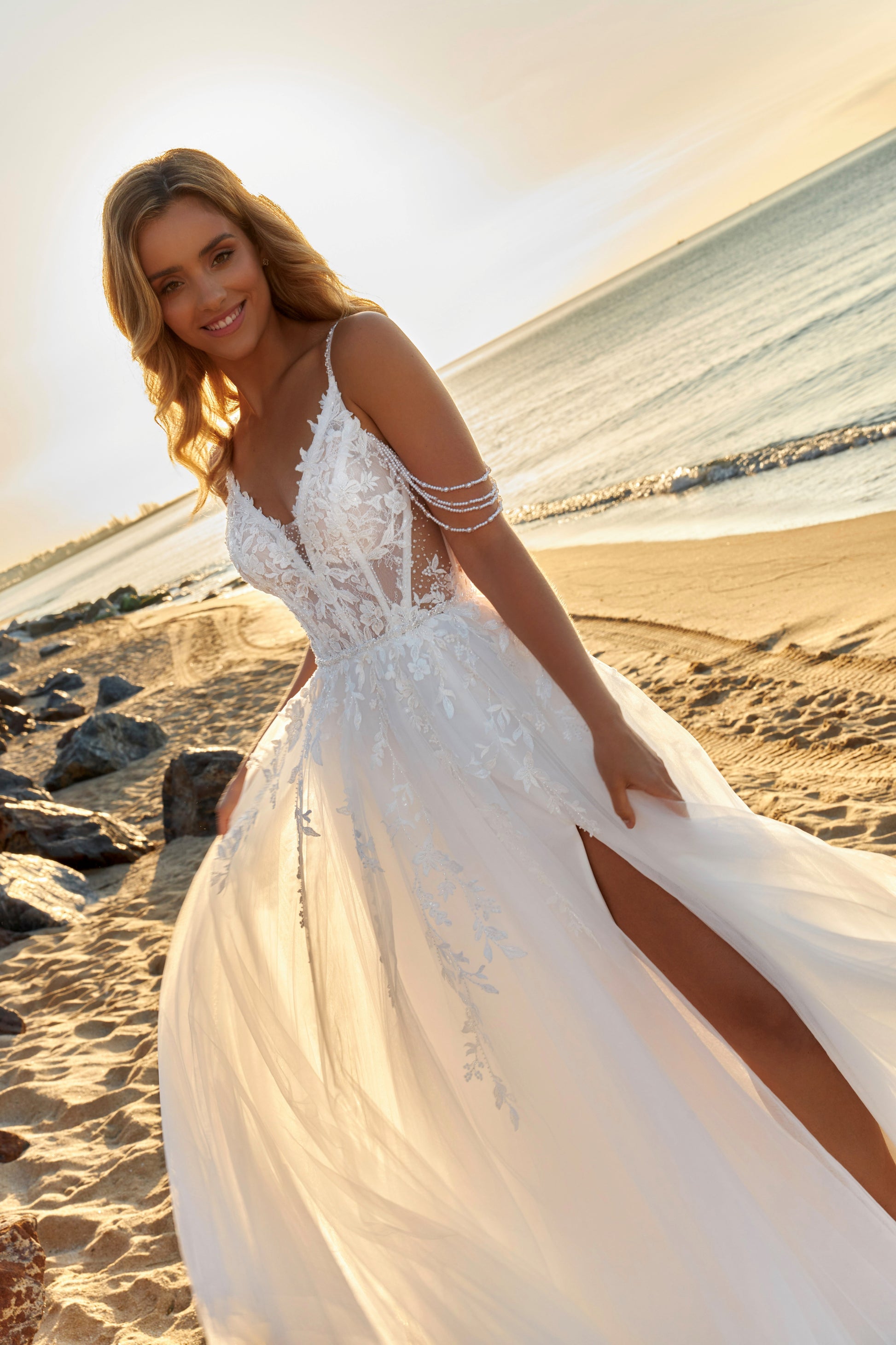 Sleeveless A-line lace bridal gown with spaghetti straps, deep-V neckline, open V-back, slit tulle skirt, and chapel train.