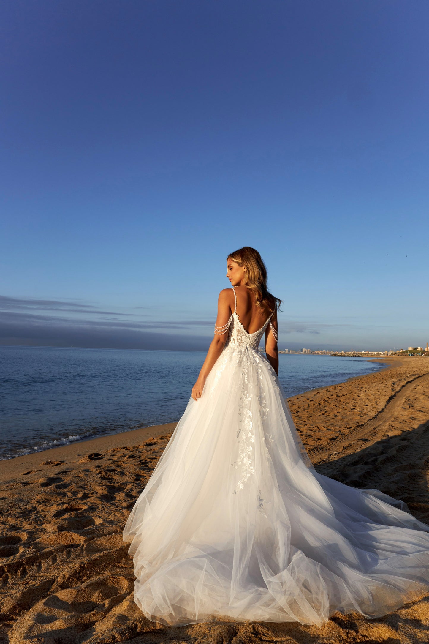 Sleeveless A-line lace bridal gown with spaghetti straps, deep-V neckline, open V-back, slit tulle skirt, and chapel train.
