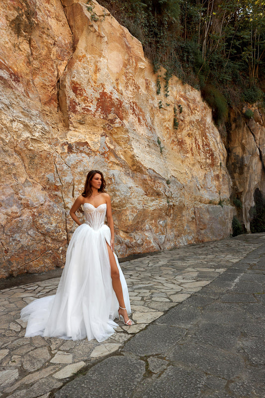Princess A-line bridal gown with sleeveless sweetheart neckline, pearl-embellished sheer bodice, drop-down waist, slit skirt, and chapel train.