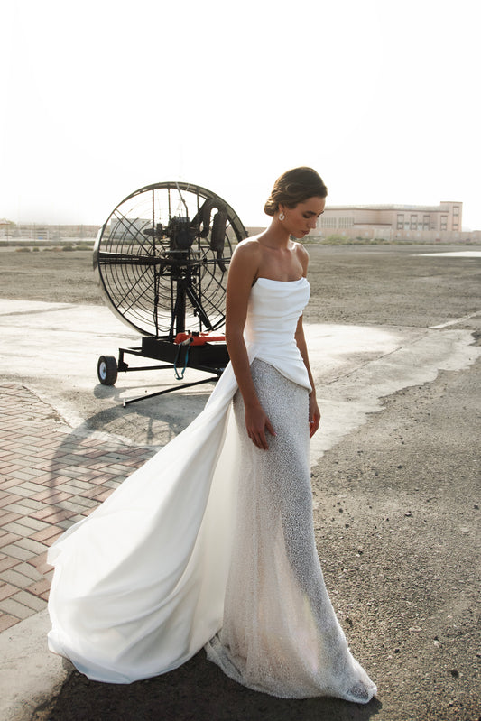 Strapless straight silhouette wedding dress with asymmetric Mikado bodice, lace skirt, zip closure, and flowing train for modern bridal style