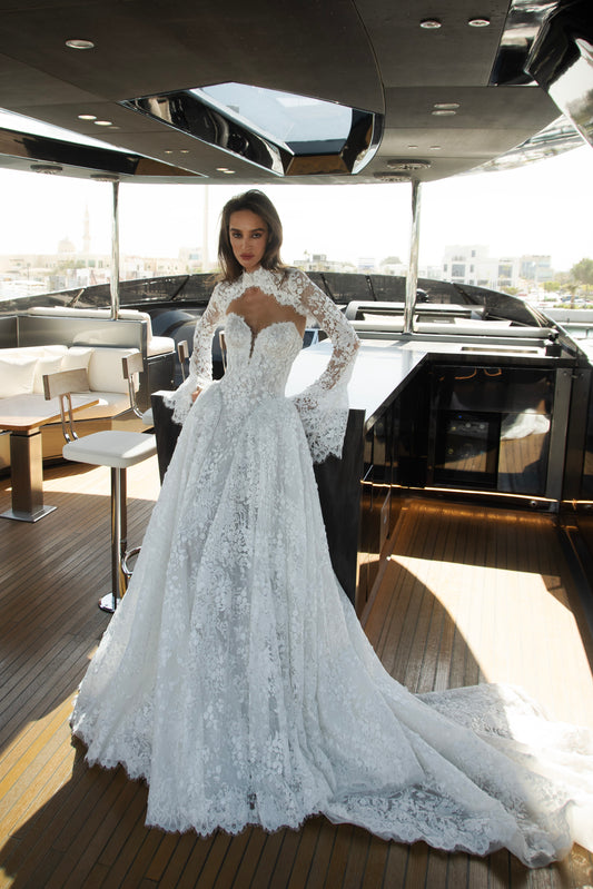 Bride wearing a high-neck lace wedding gown with long bell sleeves and chapel train from the Celeste Collection, photographed on a yacht.