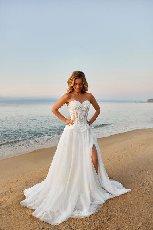 Bride in strapless lace corset wedding dress with fringe detail, lace-up back, soft tulle A-line skirt with slit, and court train.