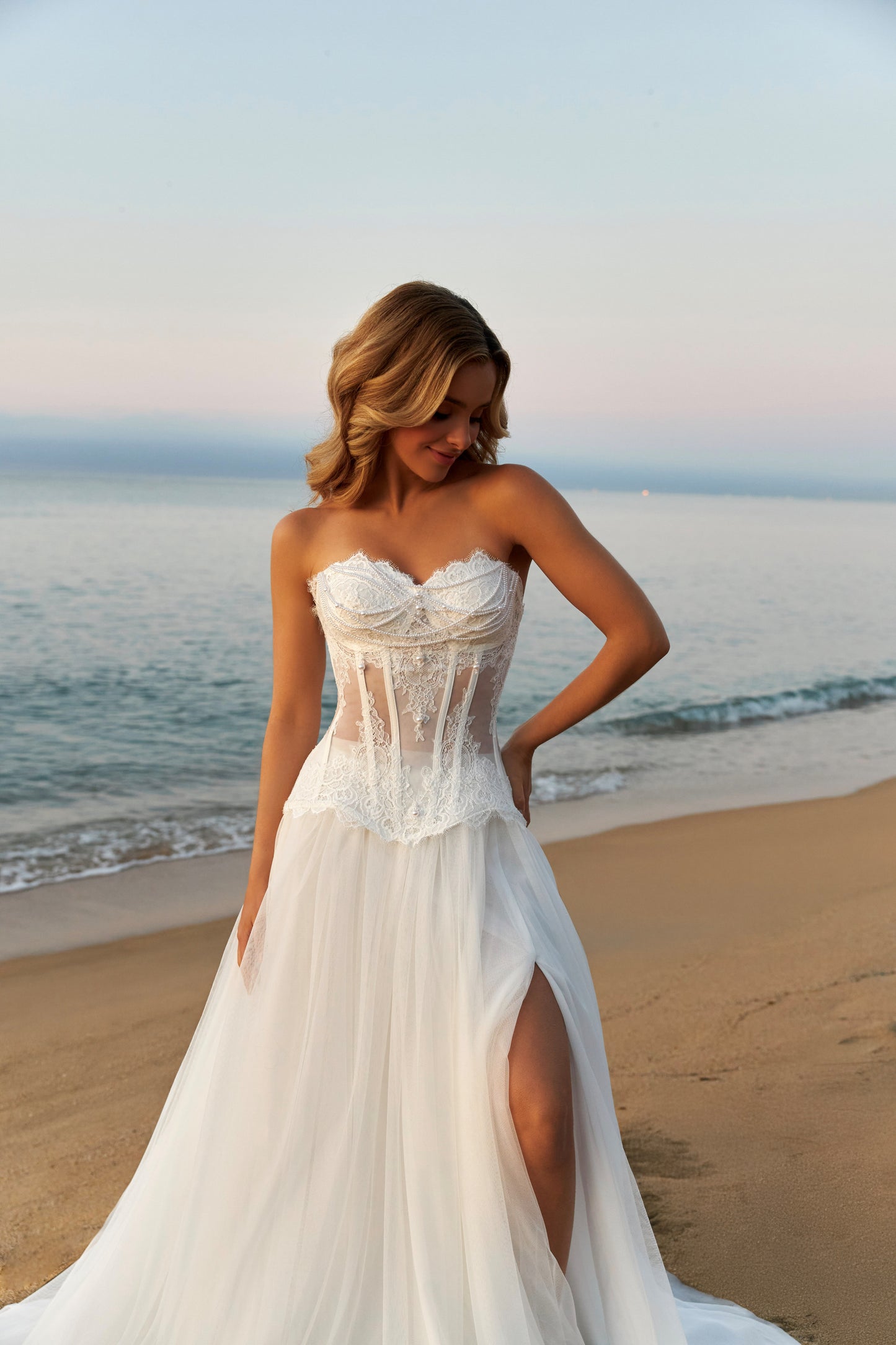 Bride in strapless lace corset wedding dress with fringe detail, lace-up back, soft tulle A-line skirt with slit, and court train.