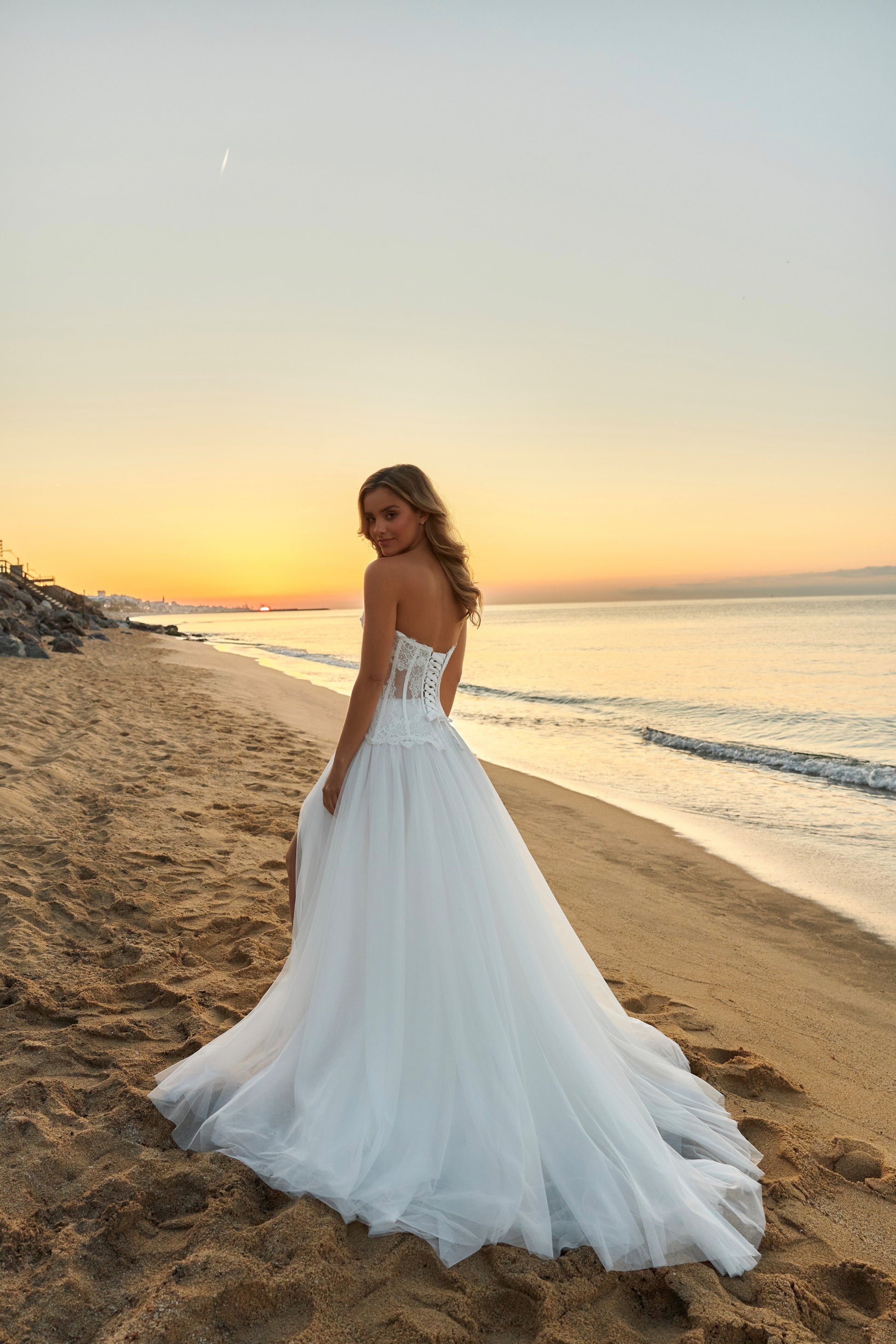 Bride in strapless lace corset wedding dress with fringe detail, lace-up back, soft tulle A-line skirt with slit, and court train.