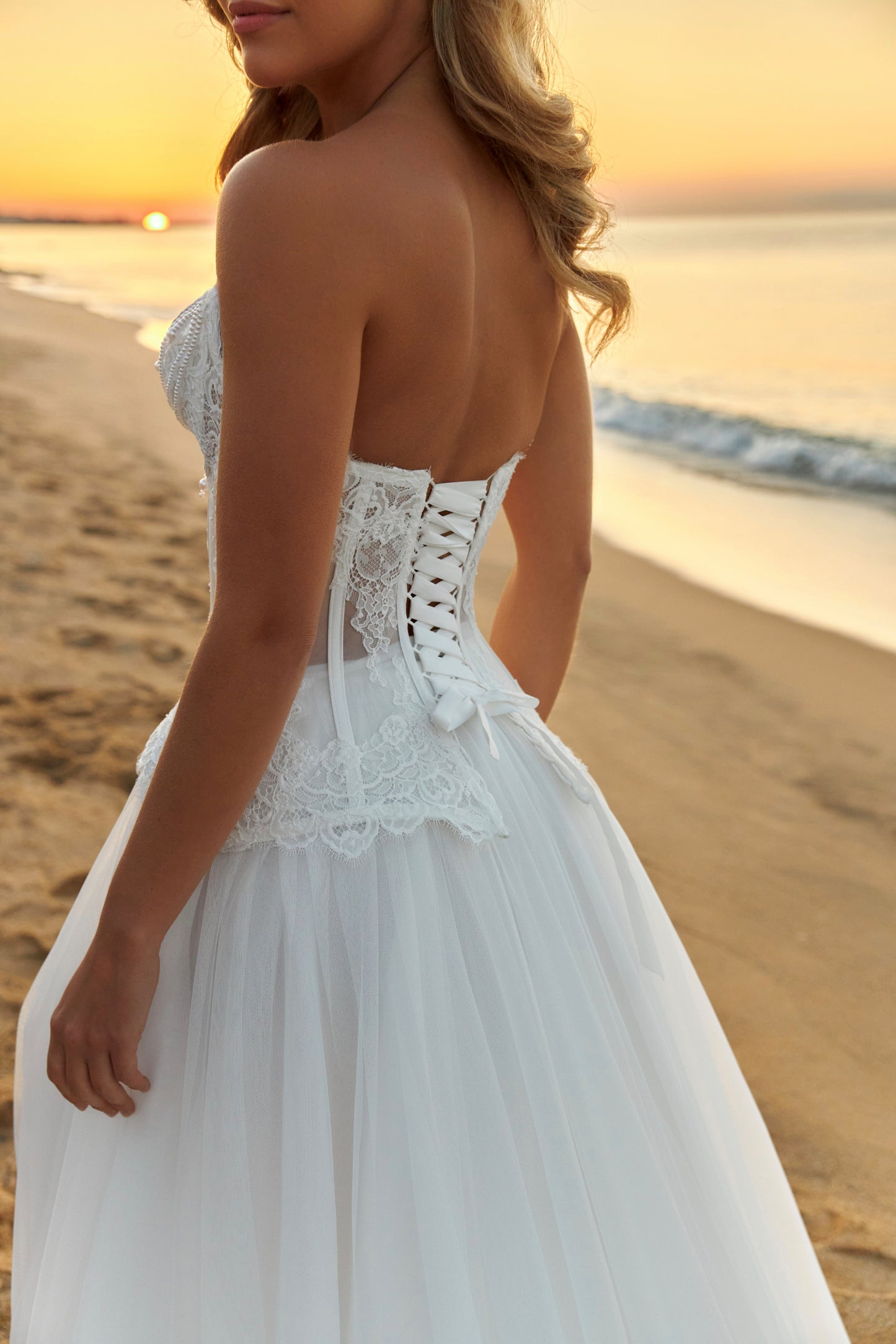 Bride in strapless lace corset wedding dress with fringe detail, lace-up back, soft tulle A-line skirt with slit, and court train.