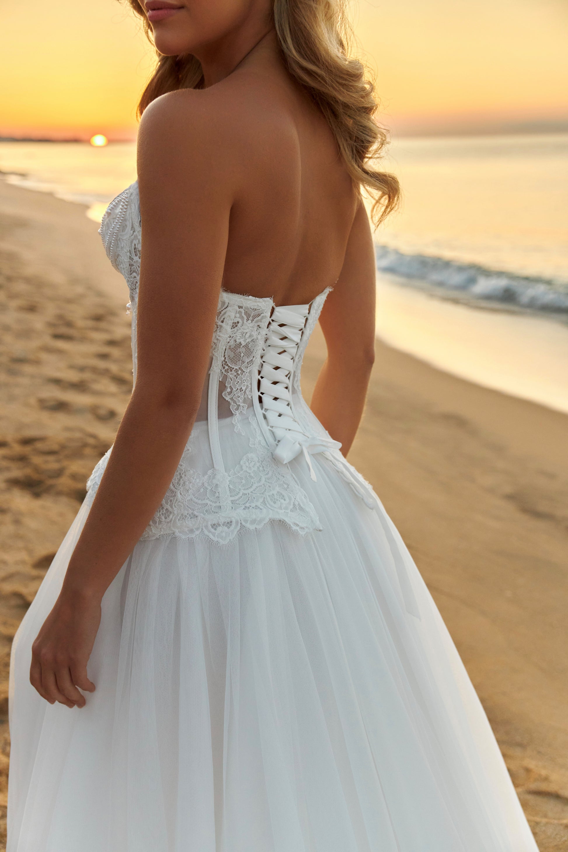 Bride in strapless lace corset wedding dress with fringe detail, lace-up back, soft tulle A-line skirt with slit, and court train.