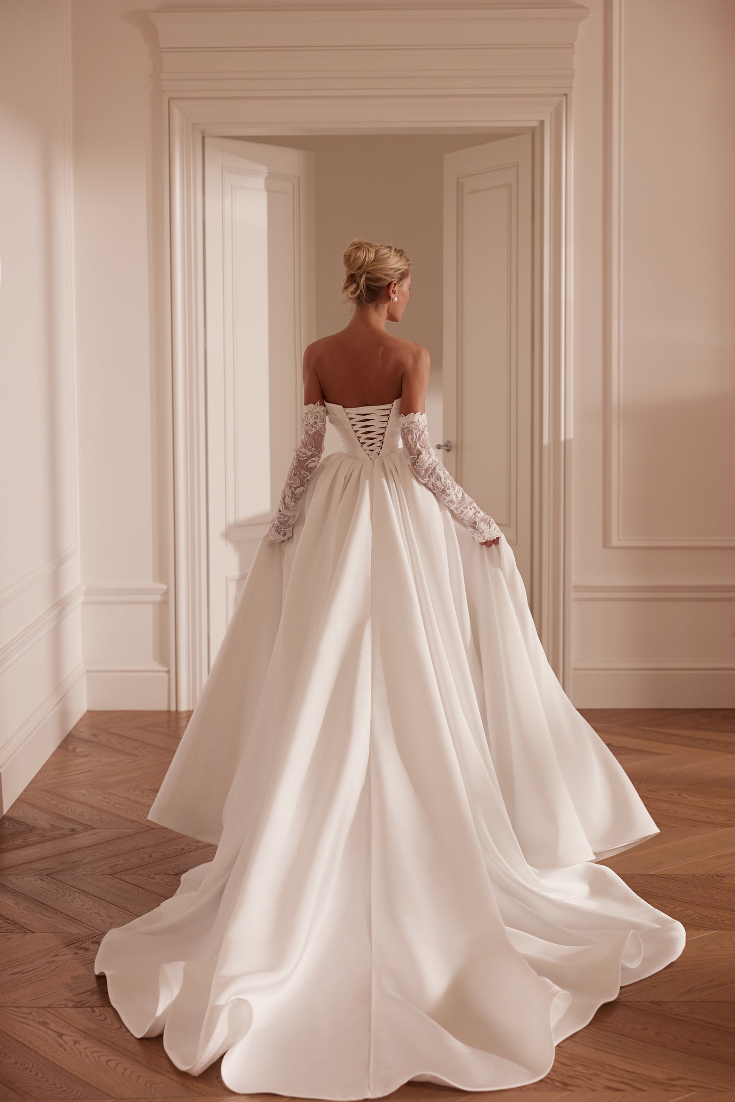 Bride wearing an off-shoulder A-line Mikado wedding dress with corset back, thigh-high slit, and chapel train.