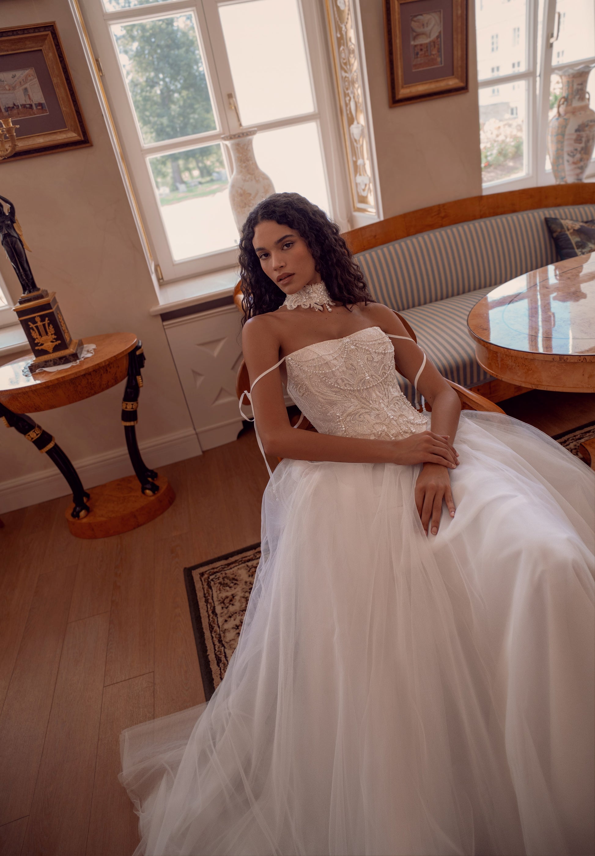 Bride wearing beaded corset A-line wedding dress with detachable tulle sleeves and flowing layered skirt.