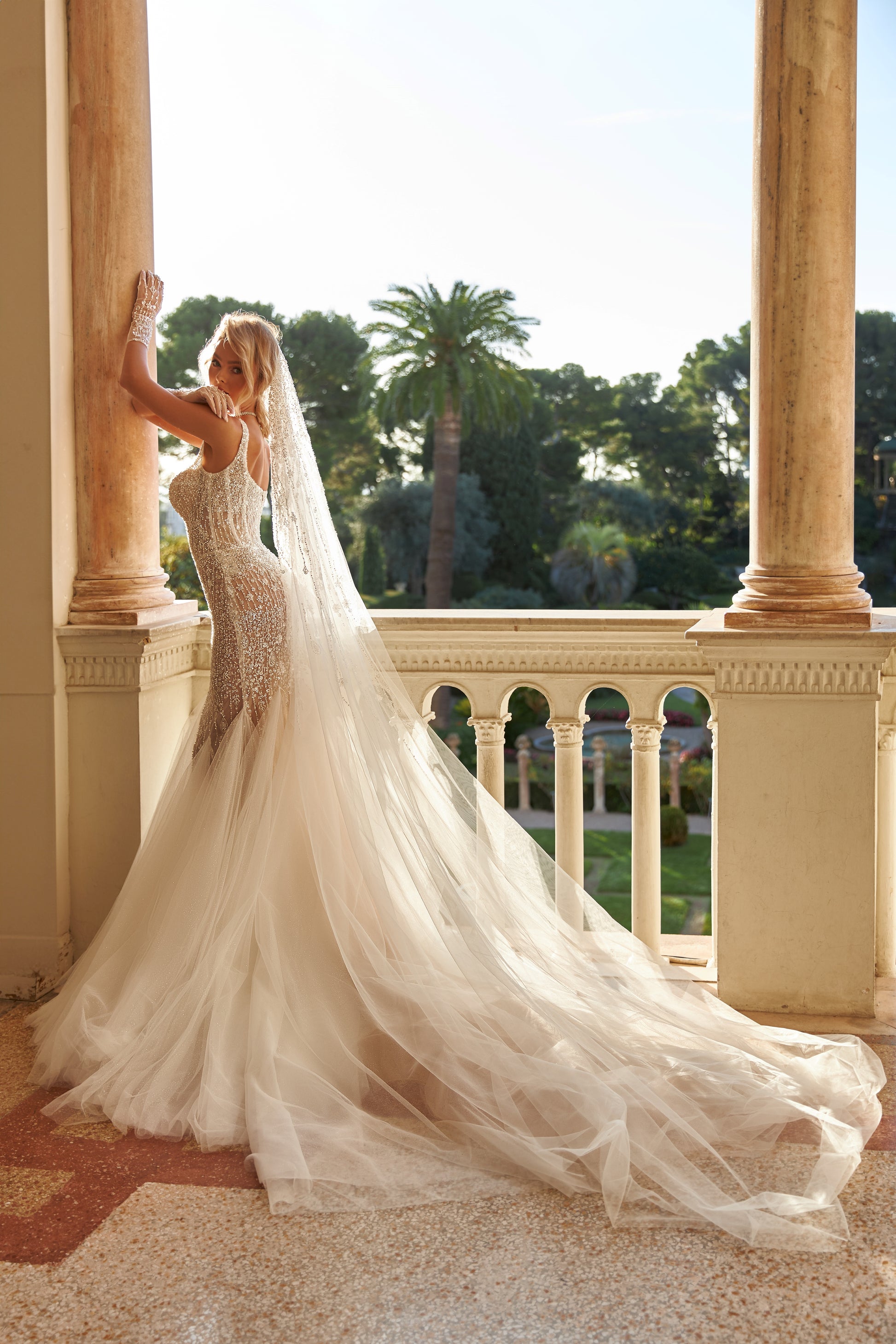 Sleeveless fitted wedding dress with square neckline, open back, lace appliques, bead and pearl embroidery, glitter tulle, and sweep court train.