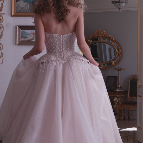 Bride wearing a pearl-embroidered corset ball gown with soft tulle skirt and flowing train.