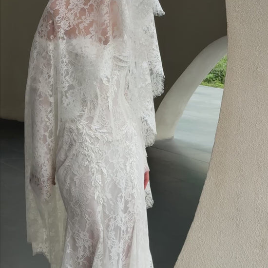 Off-shoulder lace wedding gown with long illusion sleeves, corset bodice, and chapel-length train.